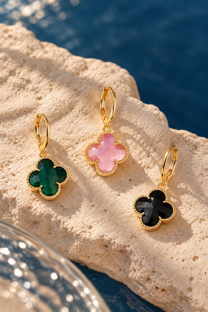 Argolas douradas com pingentes de trevo verde, rosa e preto sobre pedra clara